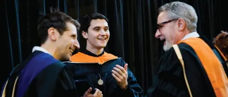 Three people smiling in a c和id commencement picture.